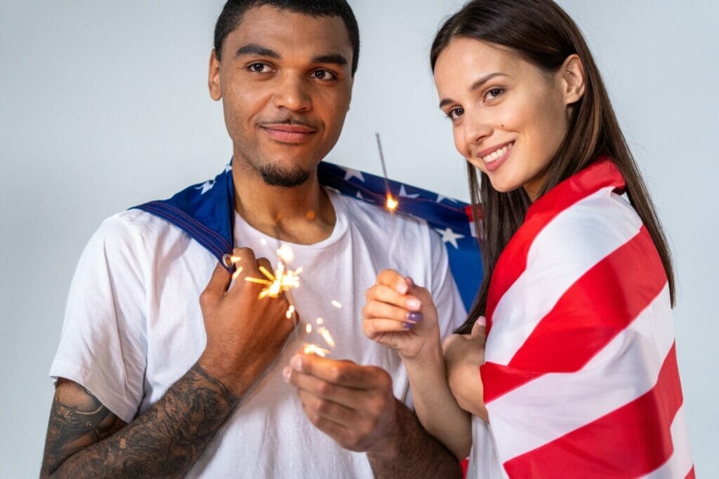 Esta nota trata sobre los requisitos para residencia americana por matrimonio. La imagen muestra a una pareja feliz con una bandera de los Estados Unidos. La imagen es solo ilustrativa 